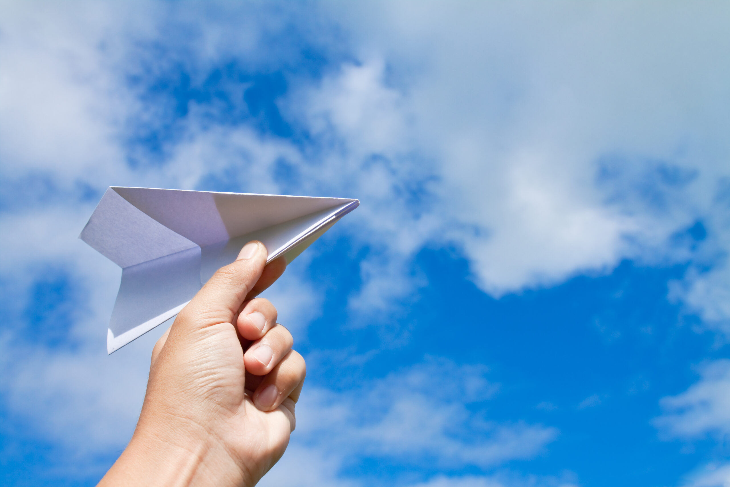 hand with paper plane against blue sky